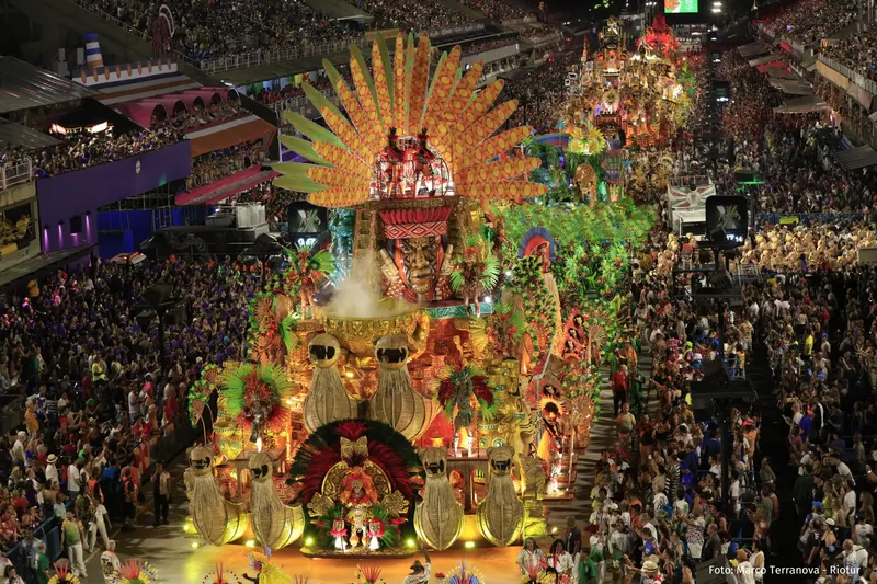 A golden float with a giant feathered headdress in front of the crowded grandstands