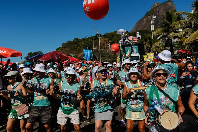 A street bloco band in matching shirts playing drums beneath Sugarloaf Mountain